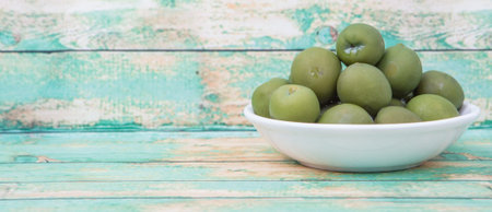 Pickled green olive in white bowl over wooden backgroundの写真素材