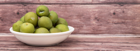 Pickled green olive in white bowl over wooden backgroundの写真素材