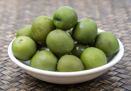 Pickled green olive in white bowl over wooden backgroundの写真素材