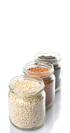 White, brown, black millet in mason jars over white backgroundの写真素材