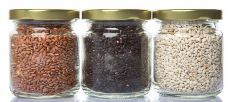 White, brown, black millet in mason jars over white backgroundの写真素材