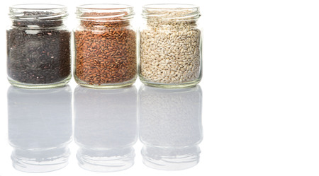 White, brown, black millet in mason jars over white backgroundの写真素材