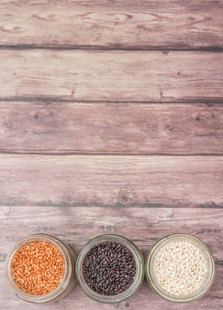 White, brown, black millet in mason jars over wooden backgroundの写真素材