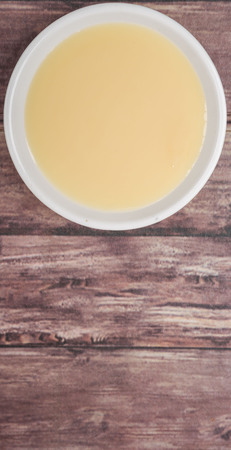 Sweet condensed milk in white bowl over wooden backgroundの写真素材