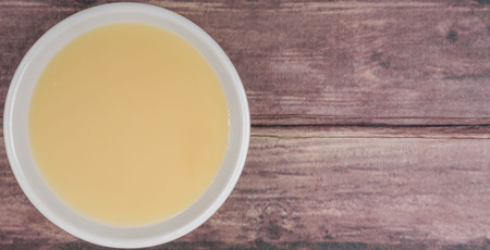 Sweet condensed milk in white bowl over wooden background
