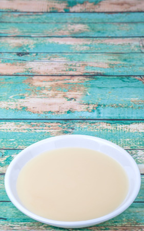 Sweet condensed milk in white bowl over wooden backgroundの写真素材