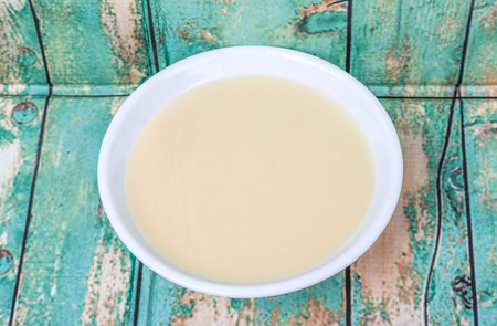 Sweet condensed milk in white bowl over wooden backgroundの写真素材