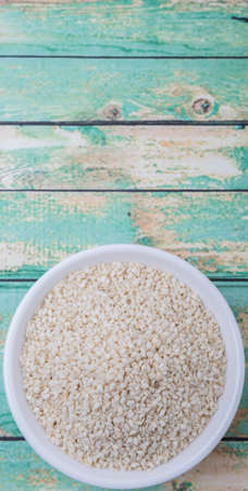 White sesame seed in white bowl over wooden background