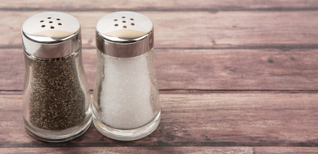 Salt and peppercorn powder in glass condiment shaker over wooden backgroundの写真素材