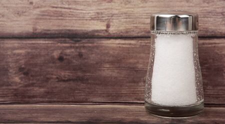 Table salt in glass condiment shaker over wooden backgroundの写真素材