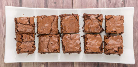 Homemade chocolate brownies in white plate over wooden background