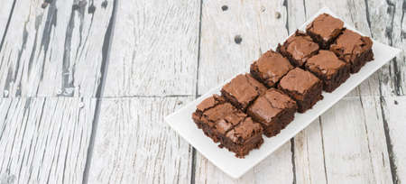 Homemade chocolate brownies in white plate over wooden background