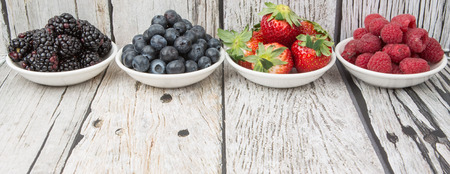 Blackberry, blueberry, strawberry and raspberry in wooden bowl over wooden backgroundの写真素材