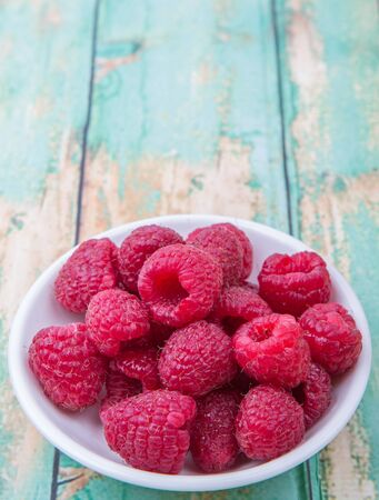 Raspberry fruit in white bowl over wooden backgroundの写真素材