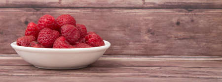 Raspberry fruit in white bowl over wooden backgroundの写真素材