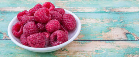 Raspberry fruit in white bowl over wooden background