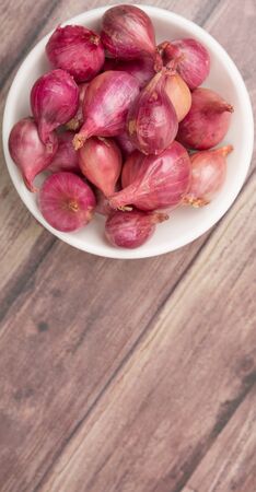 Shallots in white bowl over wooden background