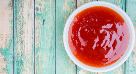 A bowl of thick chili sauce in white bowl over wooden background