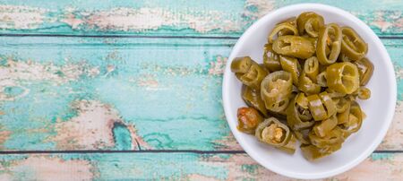 Pickled chili in white bowl over wooden background