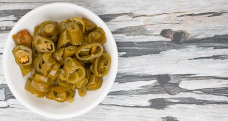 Pickled chili in white bowl over wooden background