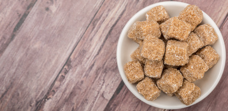Brown sugarcane cubes in white bowl over wooden backgroundの写真素材