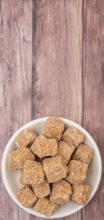 Brown sugarcane cubes in white bowl over wooden backgroundの写真素材