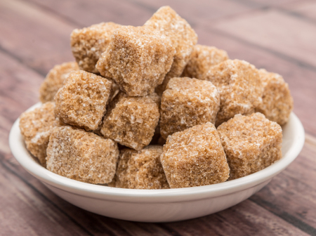 Brown sugarcane cubes in white bowl over wooden backgroundの写真素材
