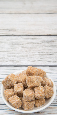 Brown sugarcane cubes in white bowl over wooden backgroundの写真素材