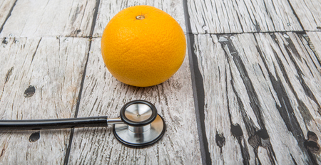 Medical stethoscope with an orange fruit. Healthy lifestyle concept image.