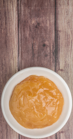 Orange fruit curd in white bowl over wooden backgroundの写真素材
