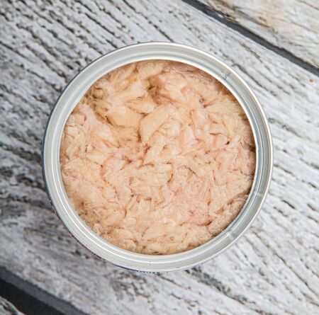 Tuna flakes in tin can over wooden background