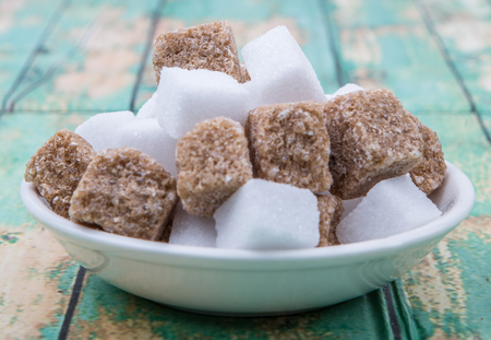 Brown and white sugar cubes in white bowl over wooden backgroundの写真素材