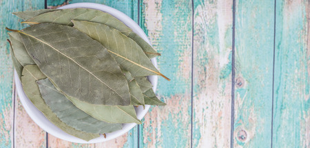 Bay leaves in white bowl over wooden background