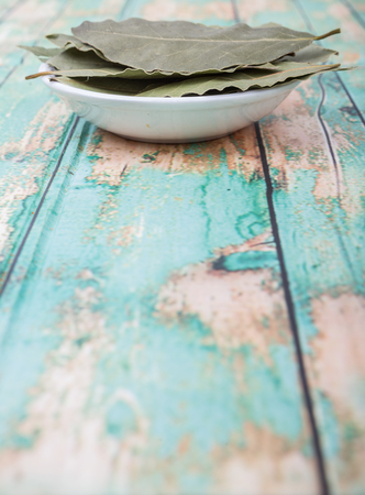 Bay leaves in white bowl over wooden background