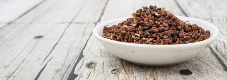 Sichuan pepper or peppercorn, also known as Chinese coriander in white bowl over wooden background