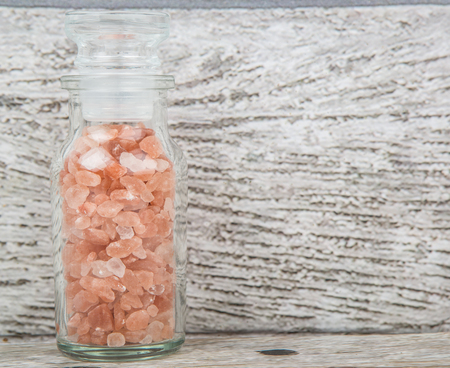 Himalaya or Himalayan rock salt in glass vial over wooden background