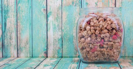 Breakfast cereal with dried raspberry fruit pieces in glass jar over wooden backgroundの写真素材