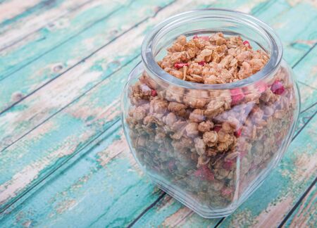Breakfast cereal with dried raspberry fruit pieces in glass jar over wooden backgroundの写真素材