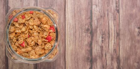 Breakfast cereal with dried raspberry fruit pieces in glass jar over wooden backgroundの写真素材