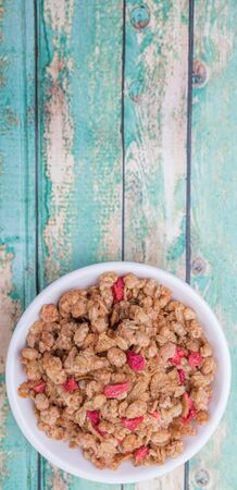 Breakfast cereal with dried raspberry fruit pieces in white bowl over wooden backgroundの写真素材