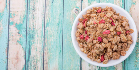 Breakfast cereal with dried raspberry fruit pieces in white bowl over wooden background