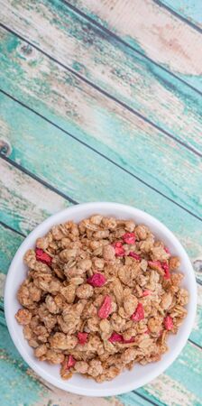 Breakfast cereal with dried raspberry fruit pieces in white bowl over wooden background