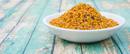 Bee pollen in white bowl over wooden background