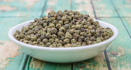 Dried green peppercorn in white bowl over wooden backgroundの写真素材