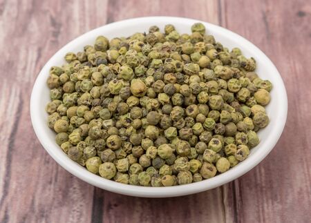 Dried green peppercorn in white bowl over wooden background