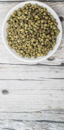 Dried green peppercorn in white bowl over wooden backgroundの写真素材