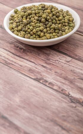 Dried green peppercorn in white bowl over wooden backgroundの写真素材