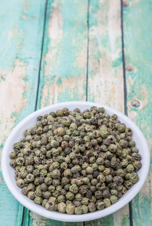 Dried green peppercorn in white bowl over wooden background