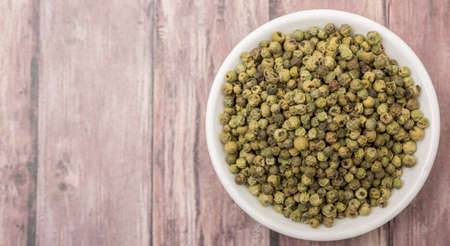 Dried green peppercorn in white bowl over wooden backgroundの写真素材