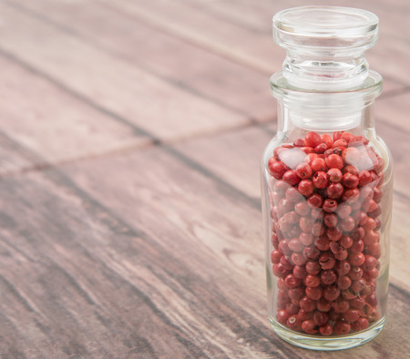 Pink peppercorn in glass vial over wooden background